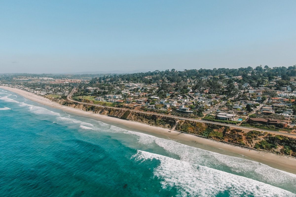 Aerial shot of waves crashing against the beach at Del Mar, with a suburban neighborhood beyond.