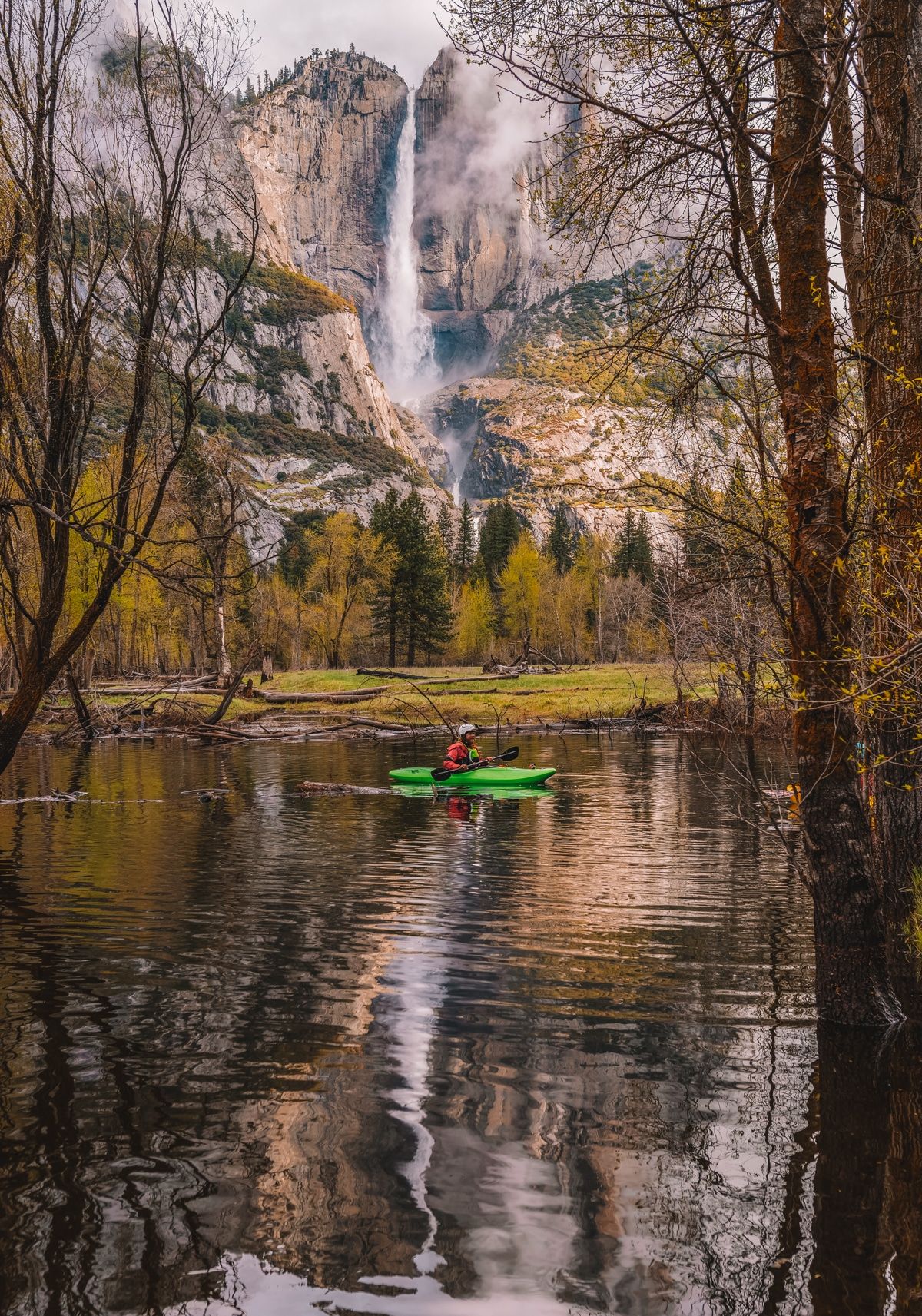 A single kayak floats on a pristine lake in the foreground and a giant waterfall cascades down a cliff-face in the distant background.