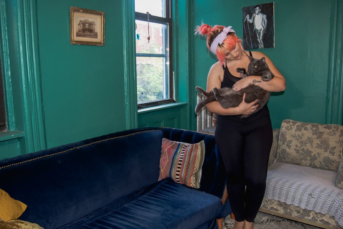 A woman holding her cat and wearing the Patitoff pet hair resistant high-waisted crossover plain leggings.