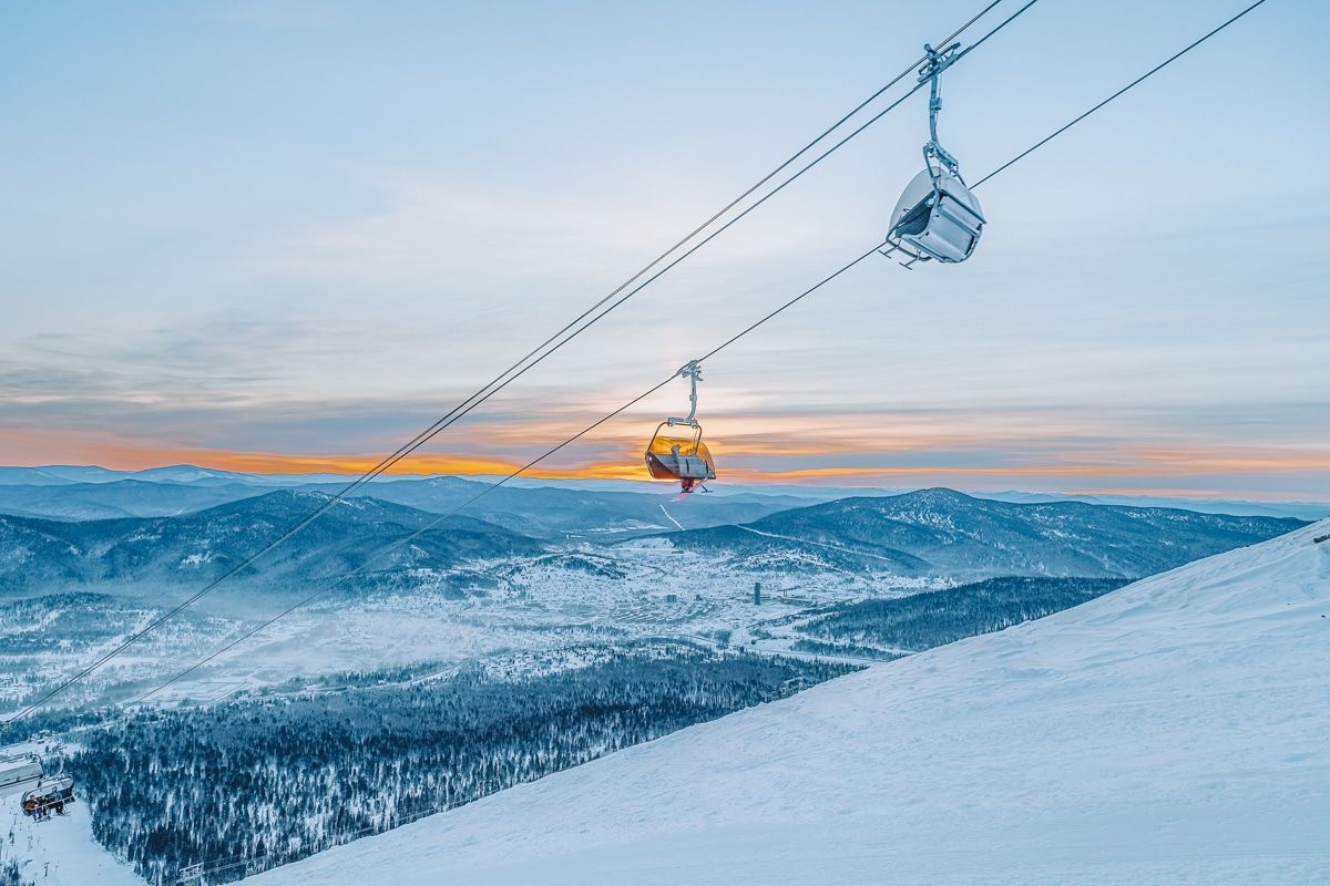 Picture of snowboarder on a ski lift with the mountains in the background.