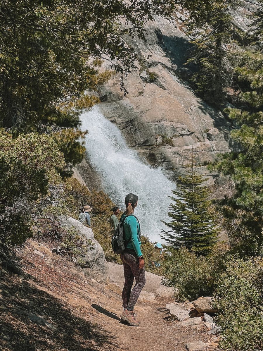 A woman standing in front of a waterfall at Yosemite National Park, after using the national park pass for entry.