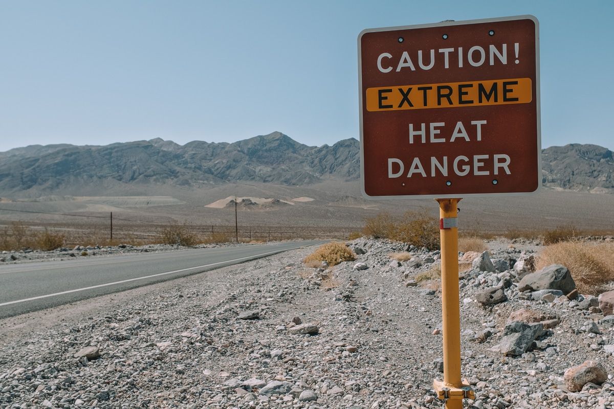 A brown summer temperature warning sign that reads, "Caution! Extreme Heat Danger" by the side of the road in Death Valley National Park