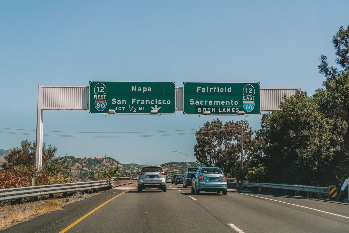 Car driving on a freeway with green signs overhead pointing to Napa, San Francisco, and Sacramento.