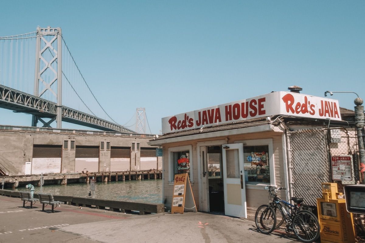 Red's Java House, a small shack on the waterfront with a vintage, red, hand-painted sign, and the Bay Bridge just beyond.