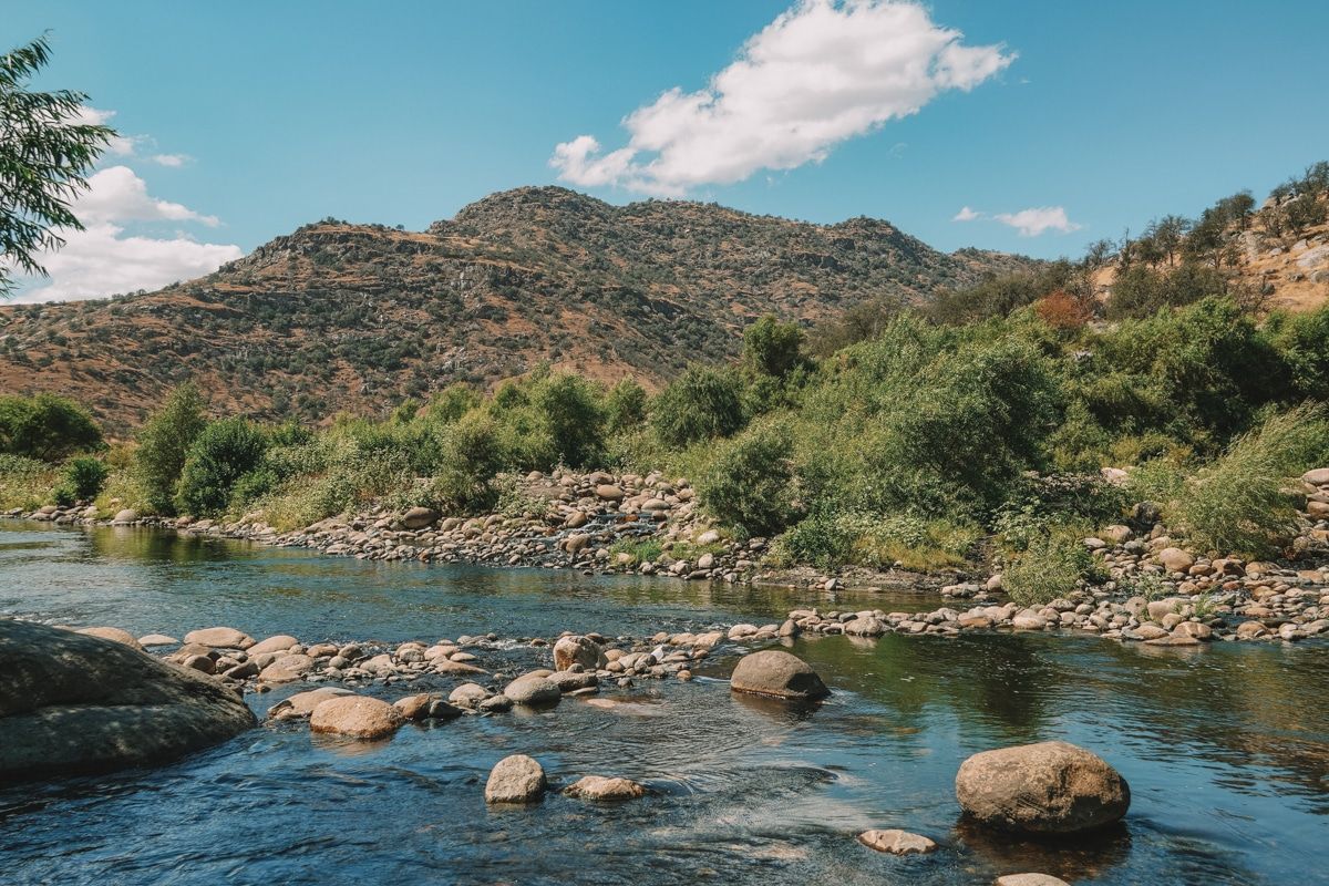 A rocky river with hills and blue sky in the background in Three Rivers, CA.