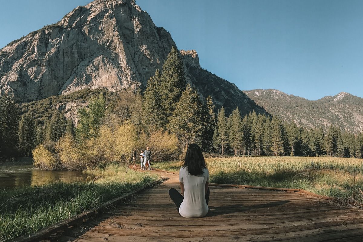 A woman in a white shirt sitting crossed-legged on the ground, looking out at Zumwalt Meadow in Kings Canyon National Park.