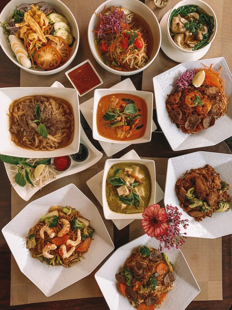 An array of Thai food dishes arranged colorfully on a wood tabletop.