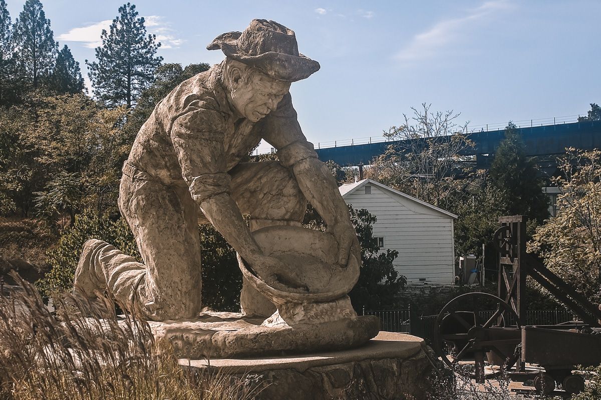 A stone statue of a miner panning for gold in a town square.