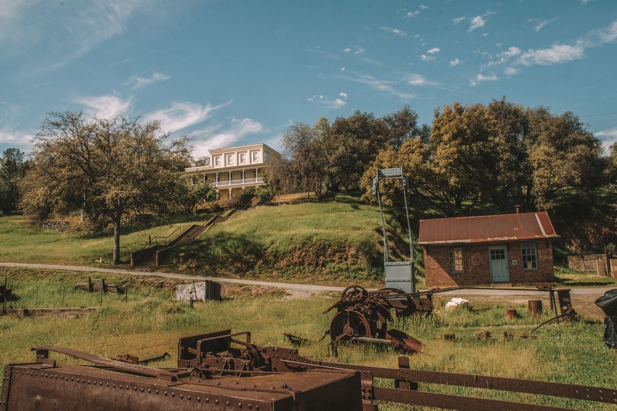 A grassy hillside in Jackson, California, with a large white manor house on the top of the hill, and rusted, antique farm equipment in the foreground.