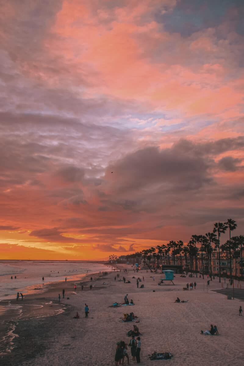 Sunset over a busy, palm tree-lined beach with a commercial strip of Restaurants in Oceanside
