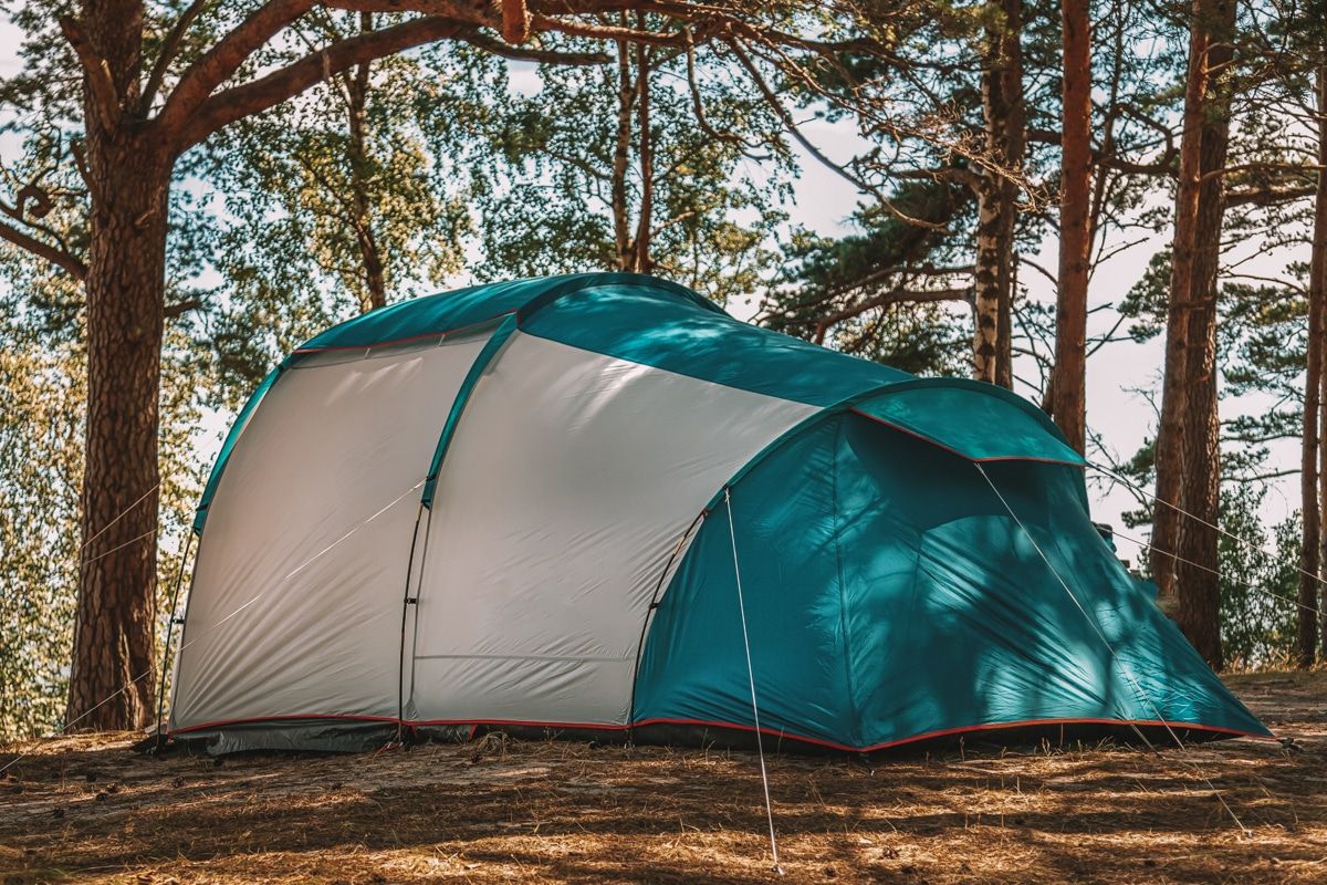 A large turquoise and grey tunnel tent pitched in a wooded campsite.