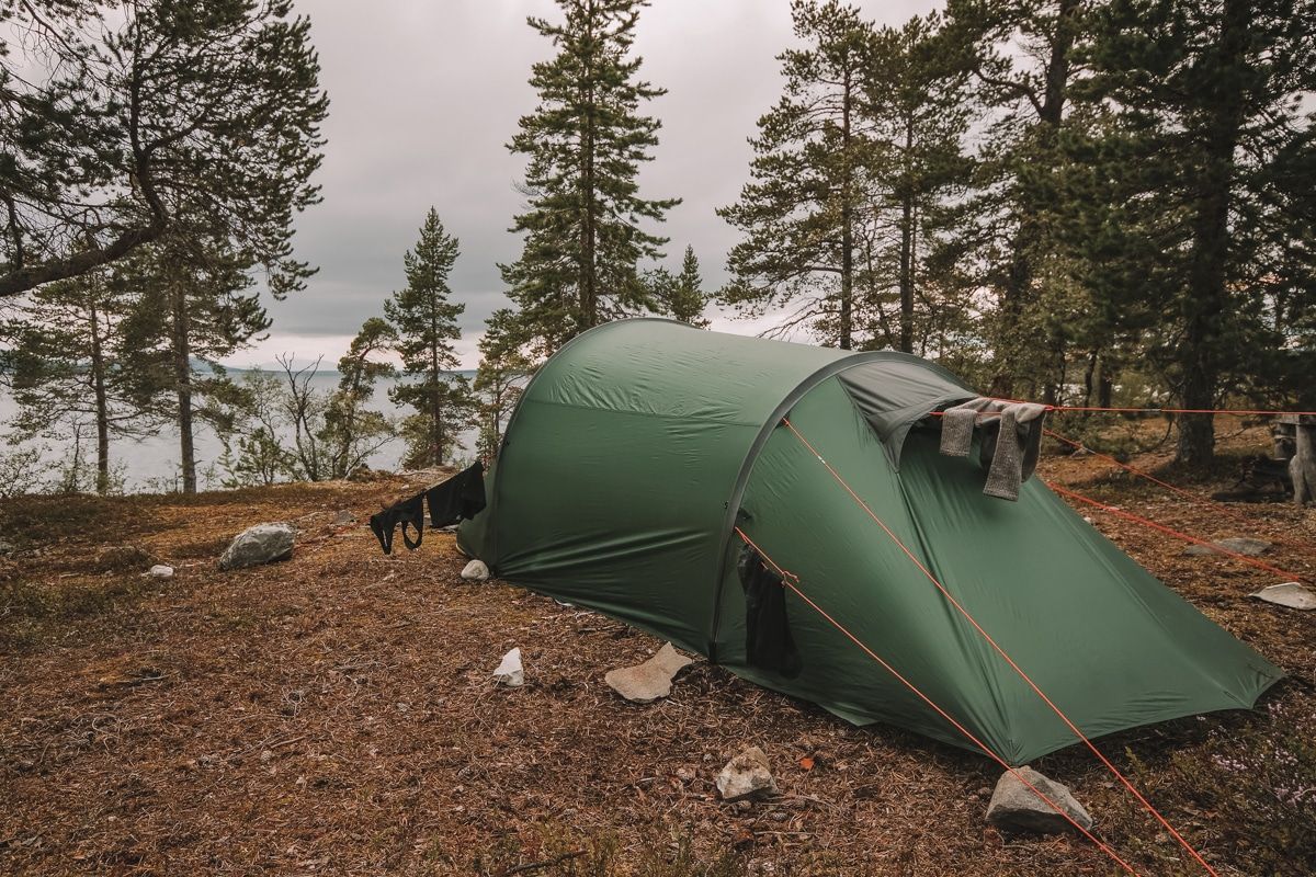 A dark green tunnel tent in a wooded campsite overlooking the ocean.