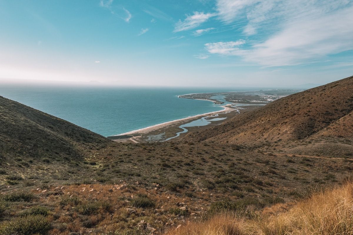 A scenic view from Mugu Peak Trail of  hillsides covered in low vegetation sloping down towards the sea on a sunny day.