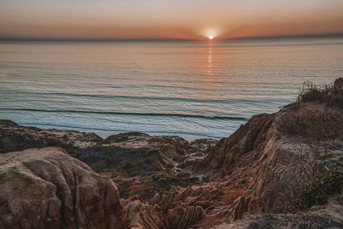 A view at sunset of sand dunes and jagged rock formations leading down to the beach from the Razor Point Trail.