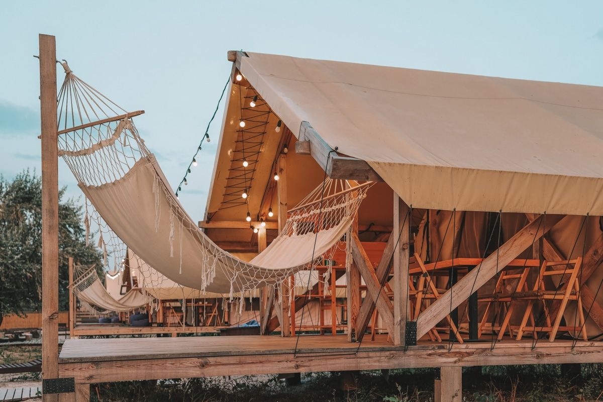 A canvas safari glamping tent on a wooden platform with a hammock in the foreground.