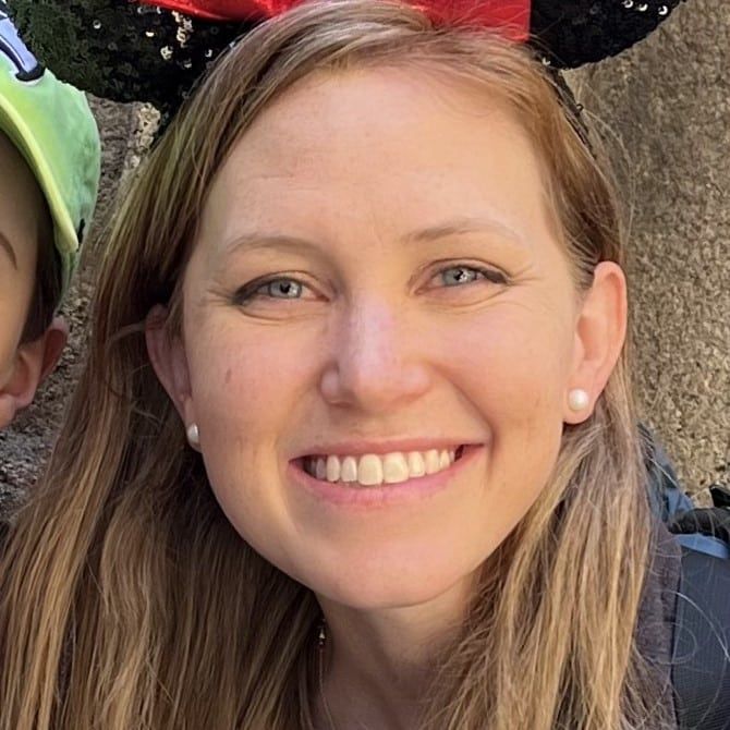 A light-haired woman smiling and wearing Minnie Mouse ears.