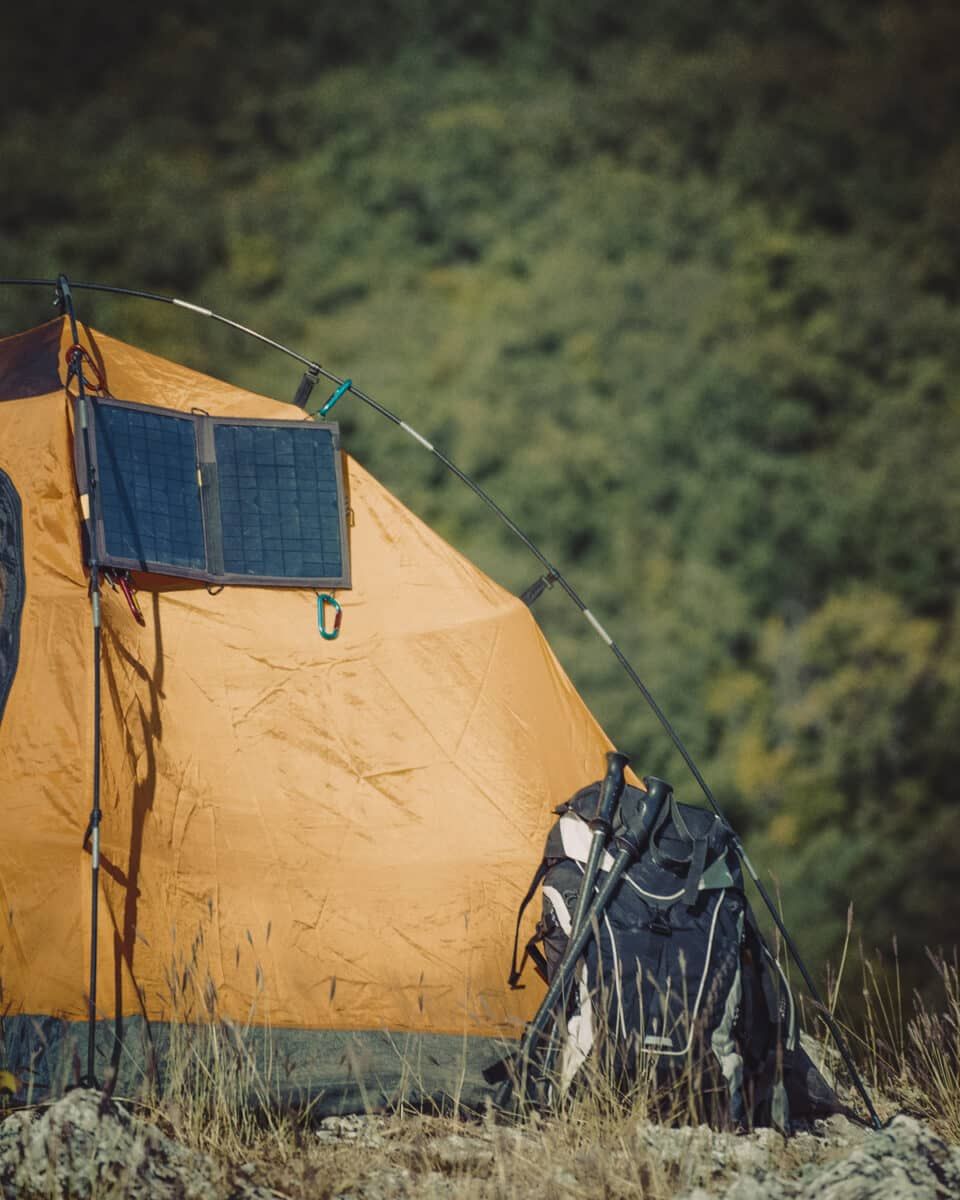The best tents With AC ports still need electrical power, evidenced here with a yellow tent that has a solar panel attached to the outside and a backpack leaning against it.