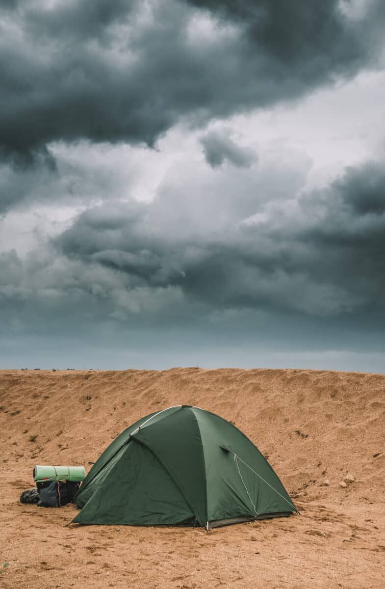 A dark green dome tent, one of the best tents for wind, pitched on the sand with a stormy looking sky overhead.
