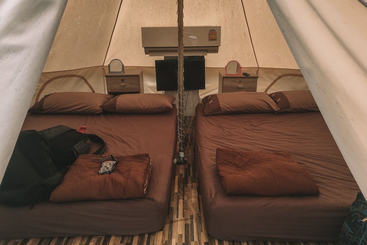 Looking in the doorway of a canvas bell tent with two double mattresses and an AC unit installed within.