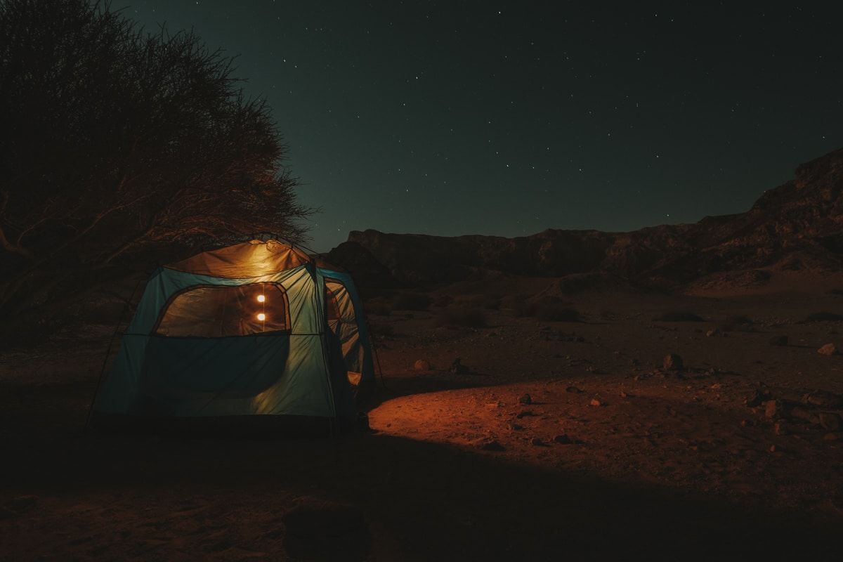 A large, blue, cabin tent illuminated against a nighttime desert landscape.