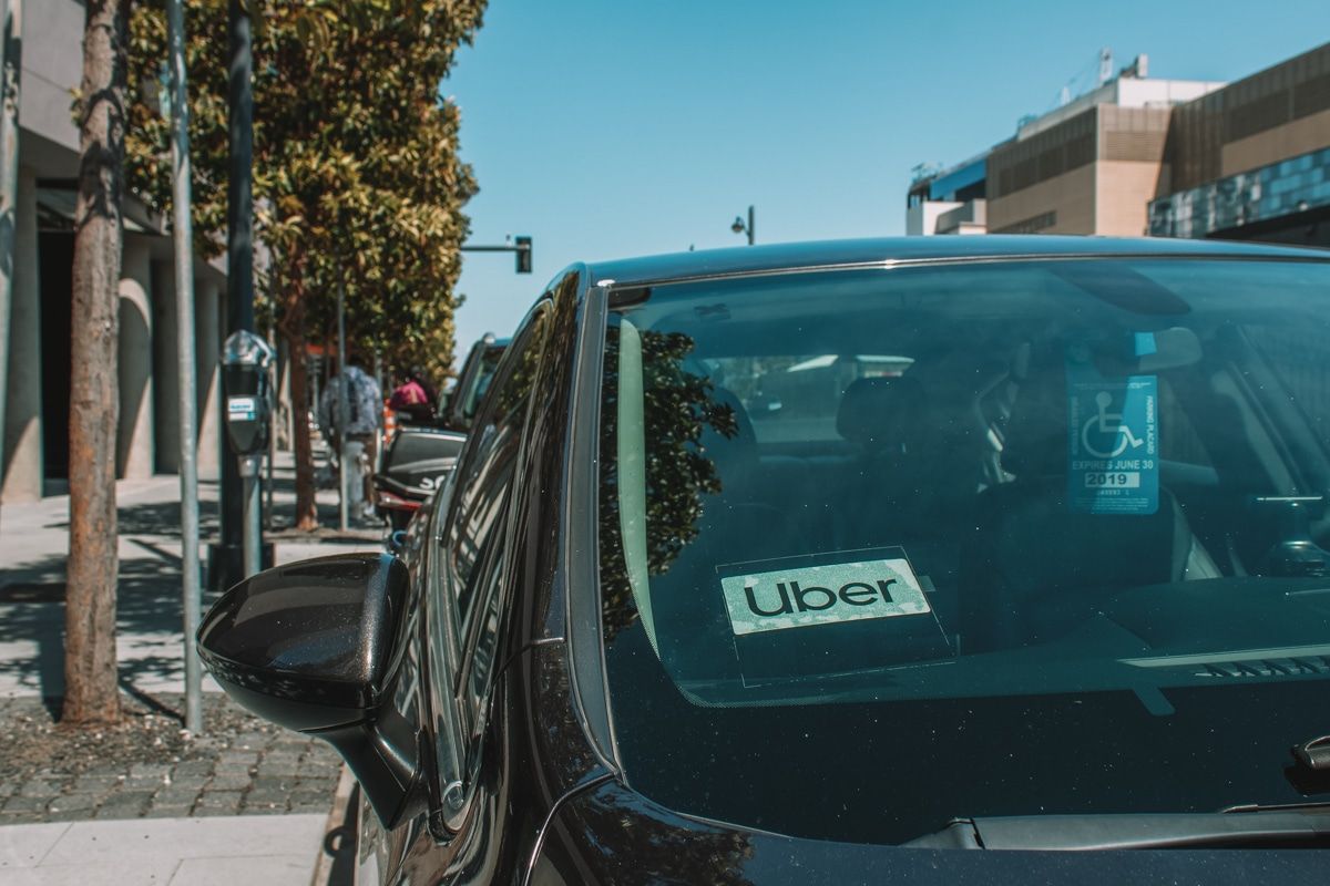 Close-up of a black car with an Uber sign in the front window, and a San Francisco city street in the background.
