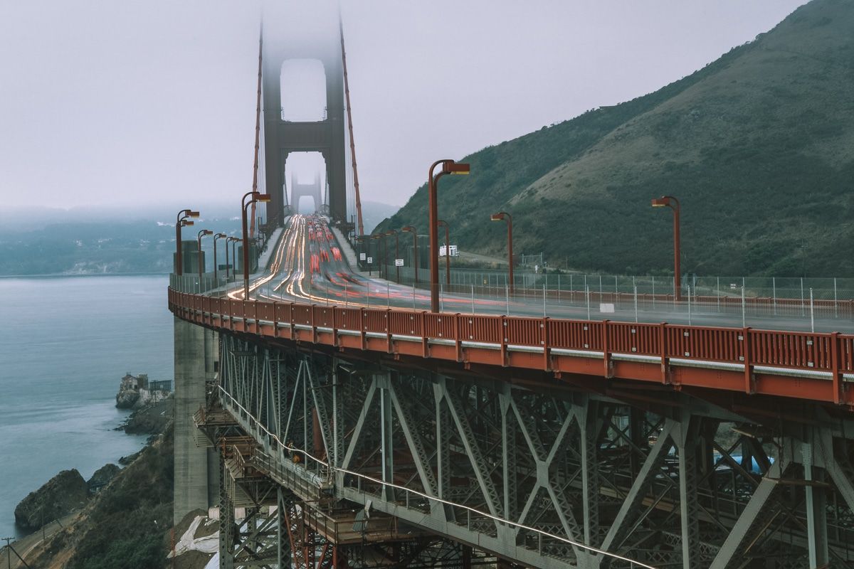 The road leading onto the Golden Gate Bridge with blurred traffic lights and fog shrouding the bridge towers.