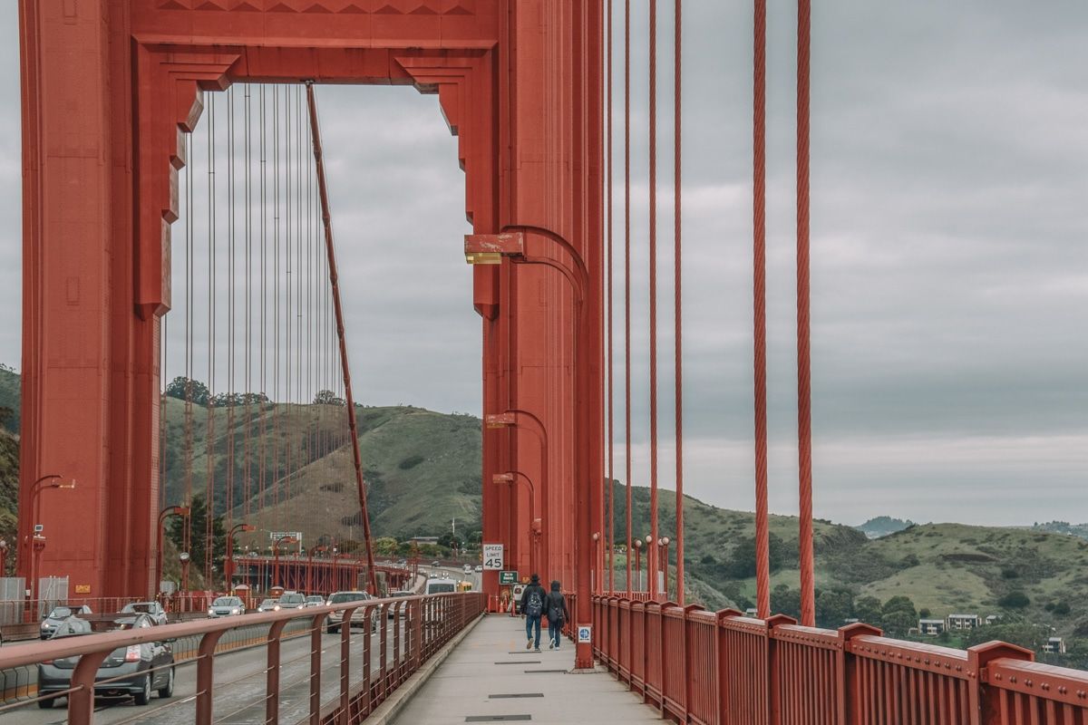 Two people seen from behind as they walk on the Golden Gate Bridge pedestrian path.