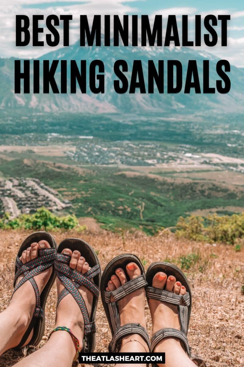 Some examples of the best minimalist hiking sandals on two pairs of women's feet at the top of a dry, grassy hill overlooking a valley and a mountain in the distance, with the text overlay, "Best Minimalist Hiking Sandals."