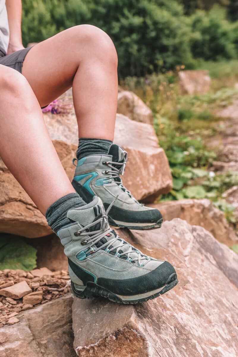 A pair of legs balanced on a boulder, wearing hiking boots and an example of some of the best summer hiking socks in grey.