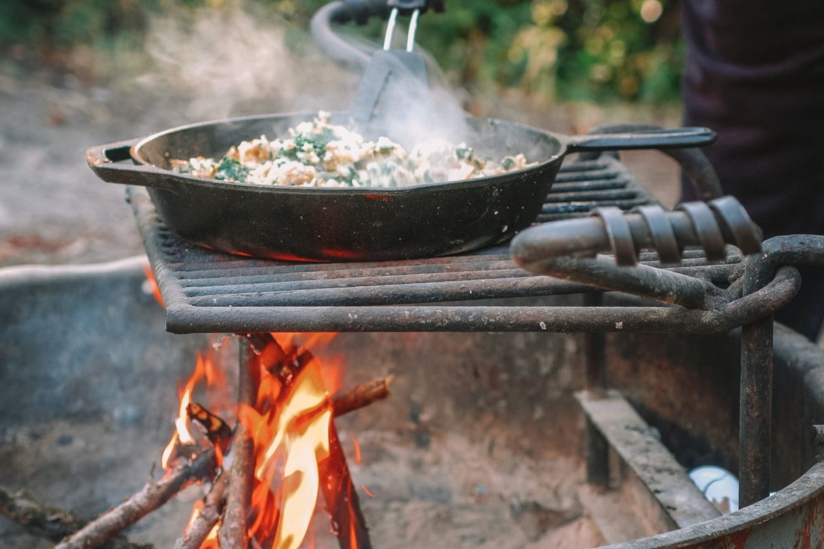 A steaming scramble cooking in a cast iron skillet over a campfire.