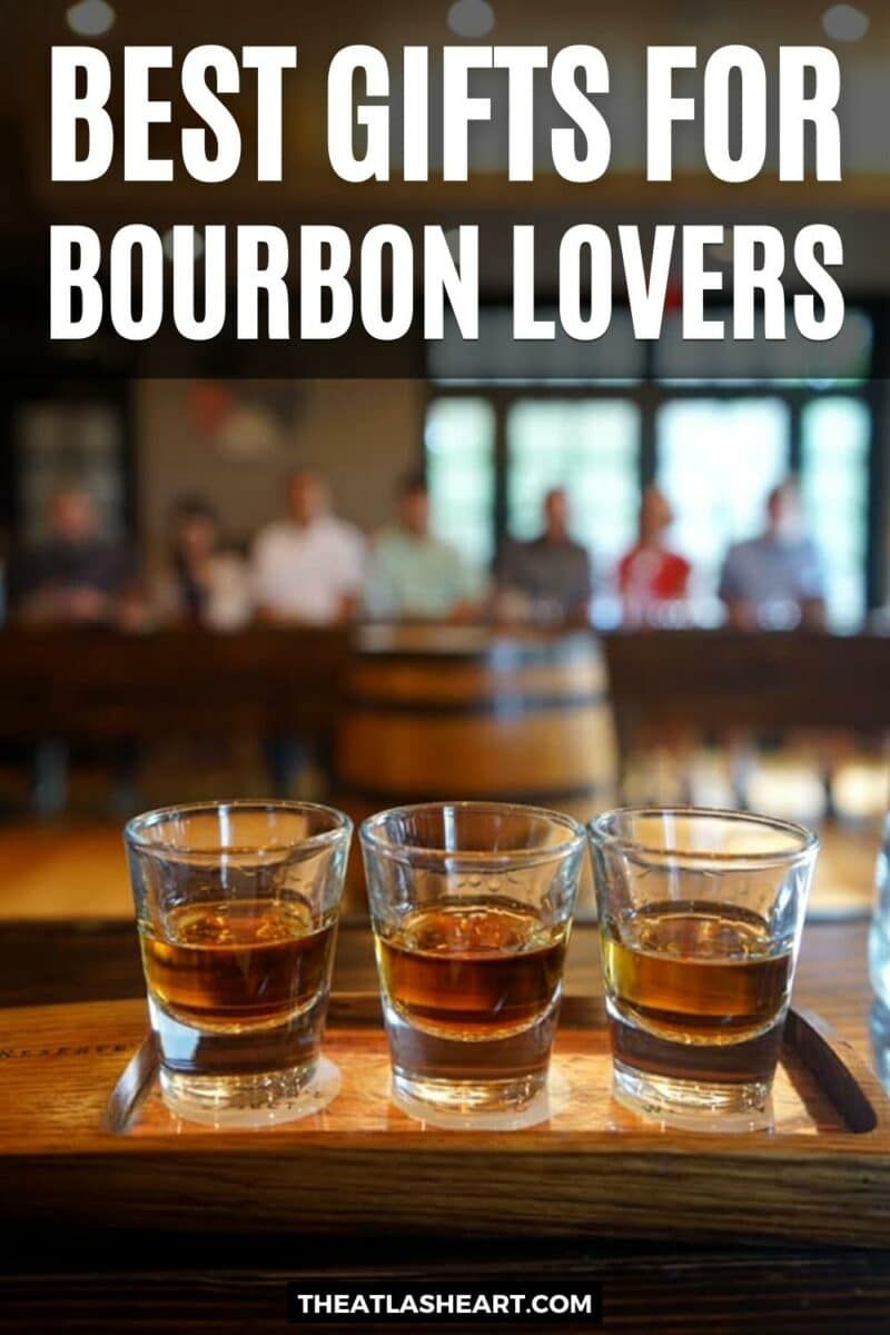 Three shots of bourbon lined up on a wooden surface with a soft-focus tasting room in the background with the text overlay, "Best Gifts for Bourbon Lovers."