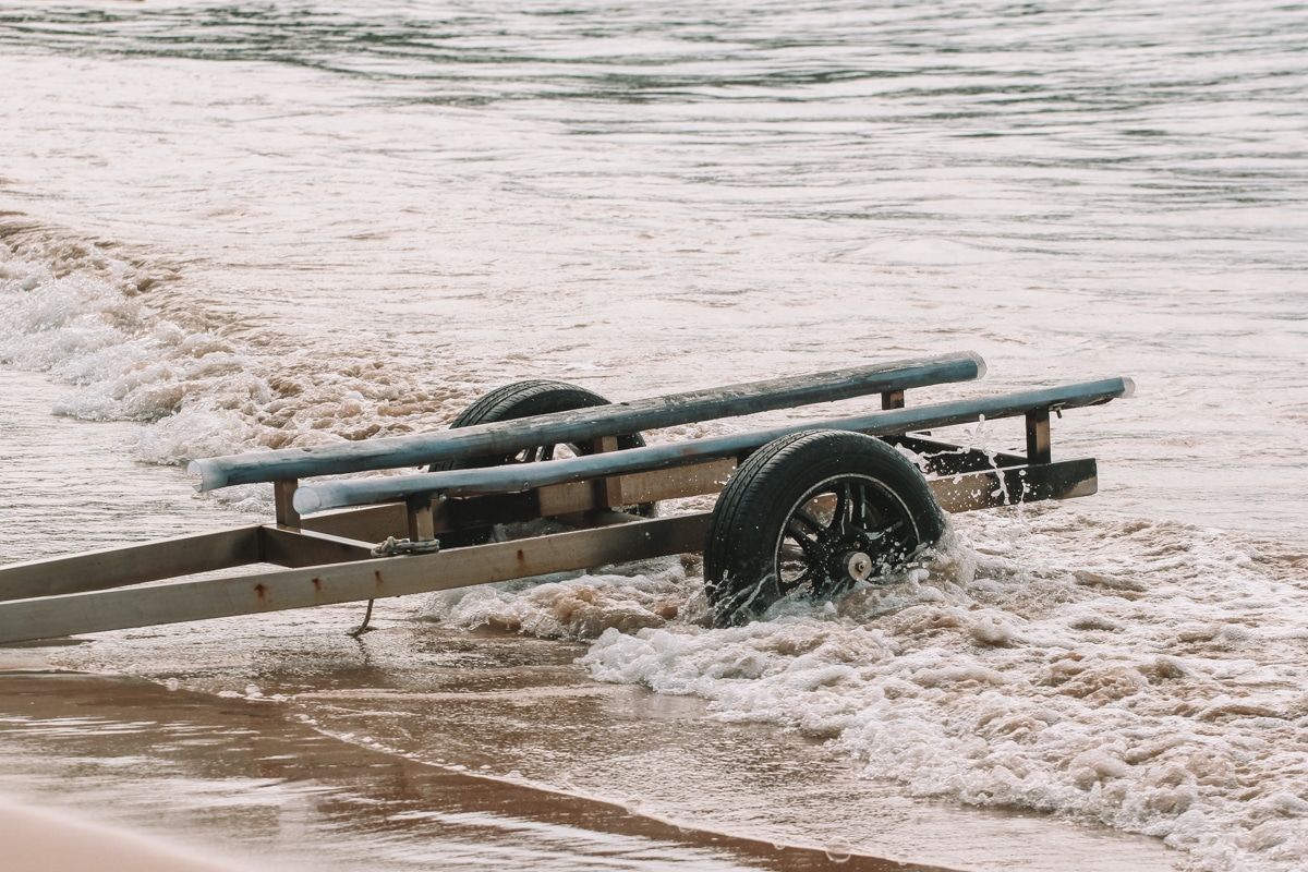 A two-wheeled boat trailer sitting in some waves on a sandy beach.