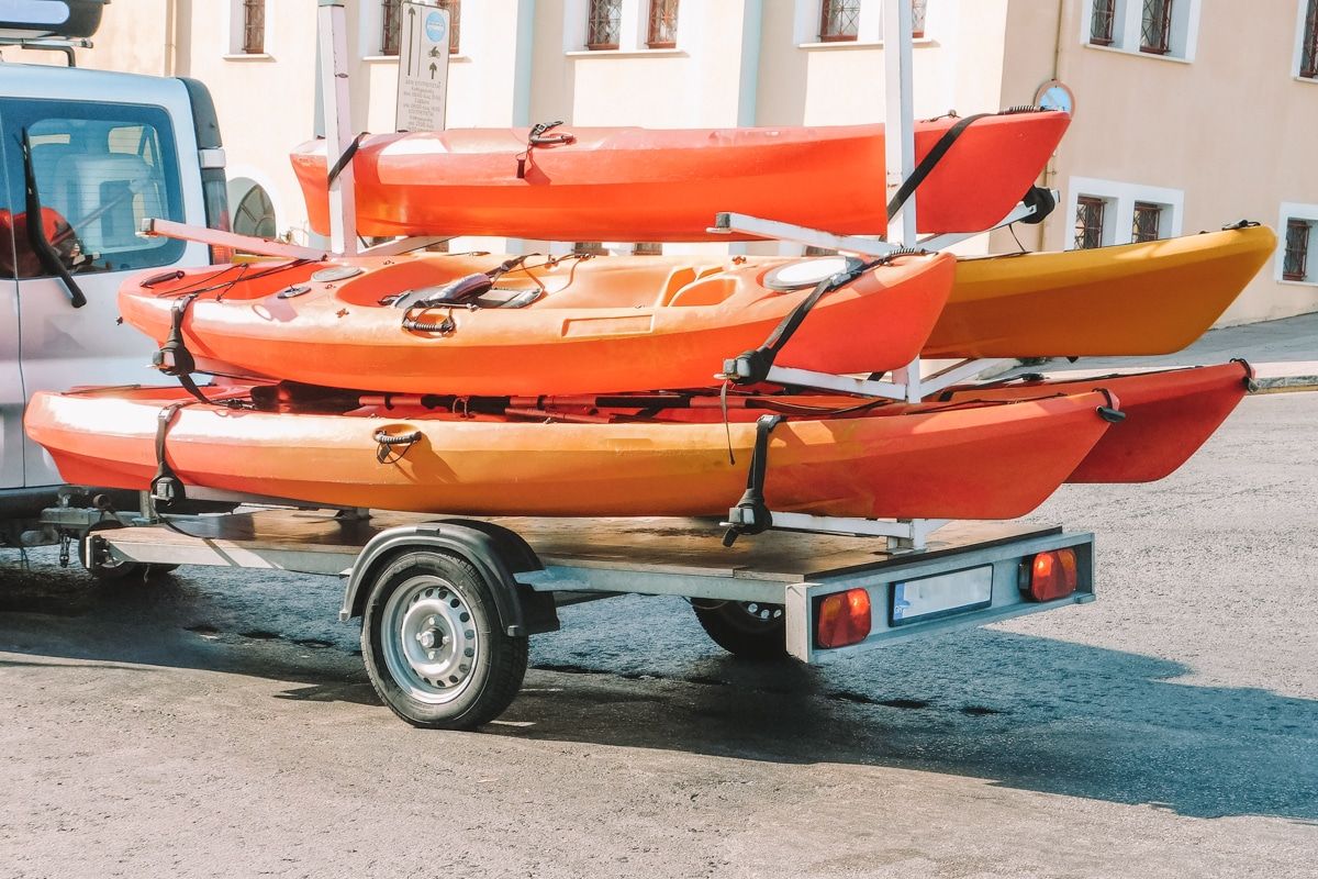 Five orange kayaks strapped onto a kayak trailer driving down a city street.
