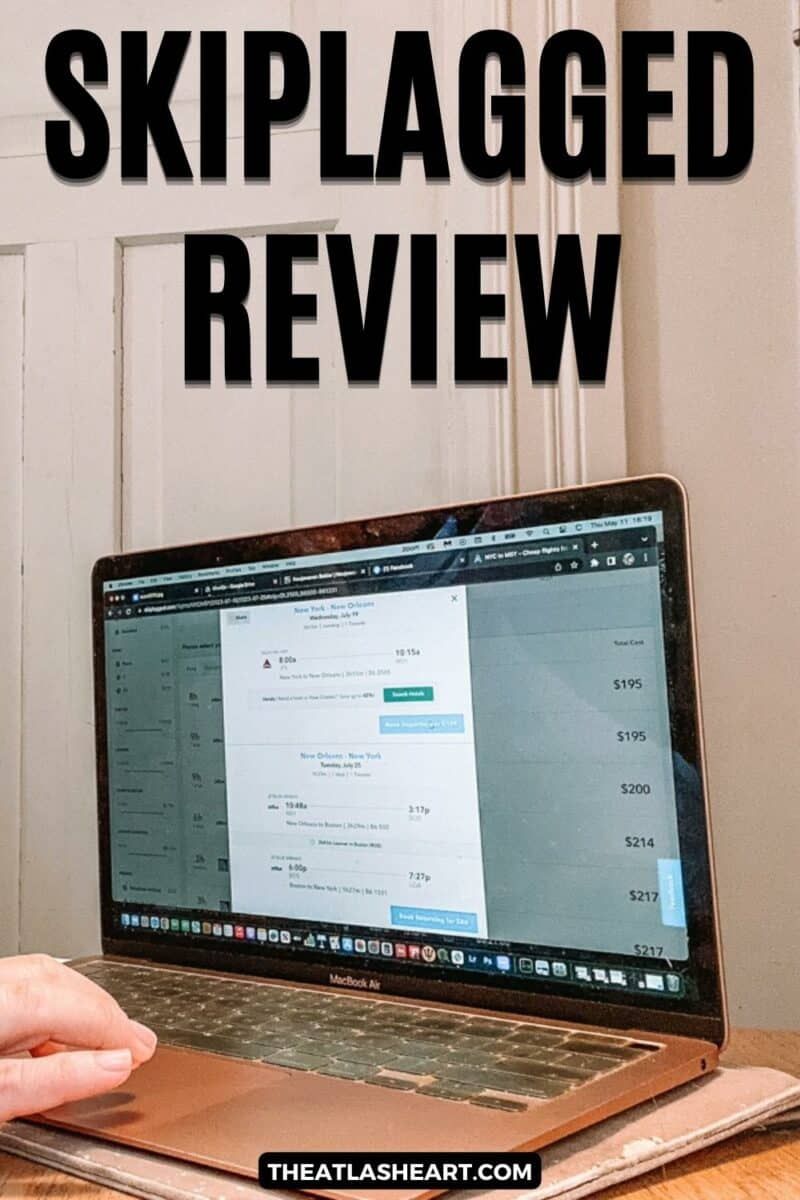 A rose gold macbook laptop displaying the Skiplagged homepage sits on a wooden desk with a closed white door in the background and a hand scrolling on the trackpad in the foreground. with the text overlay, "Skiplagged Review."