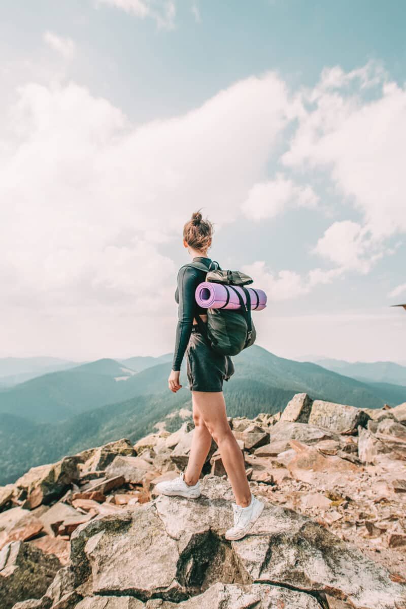The best hiking underwear for women: a young woman wearing shorts and a hiking backpack standing on a rocky vista point, looking away over her shoulder.