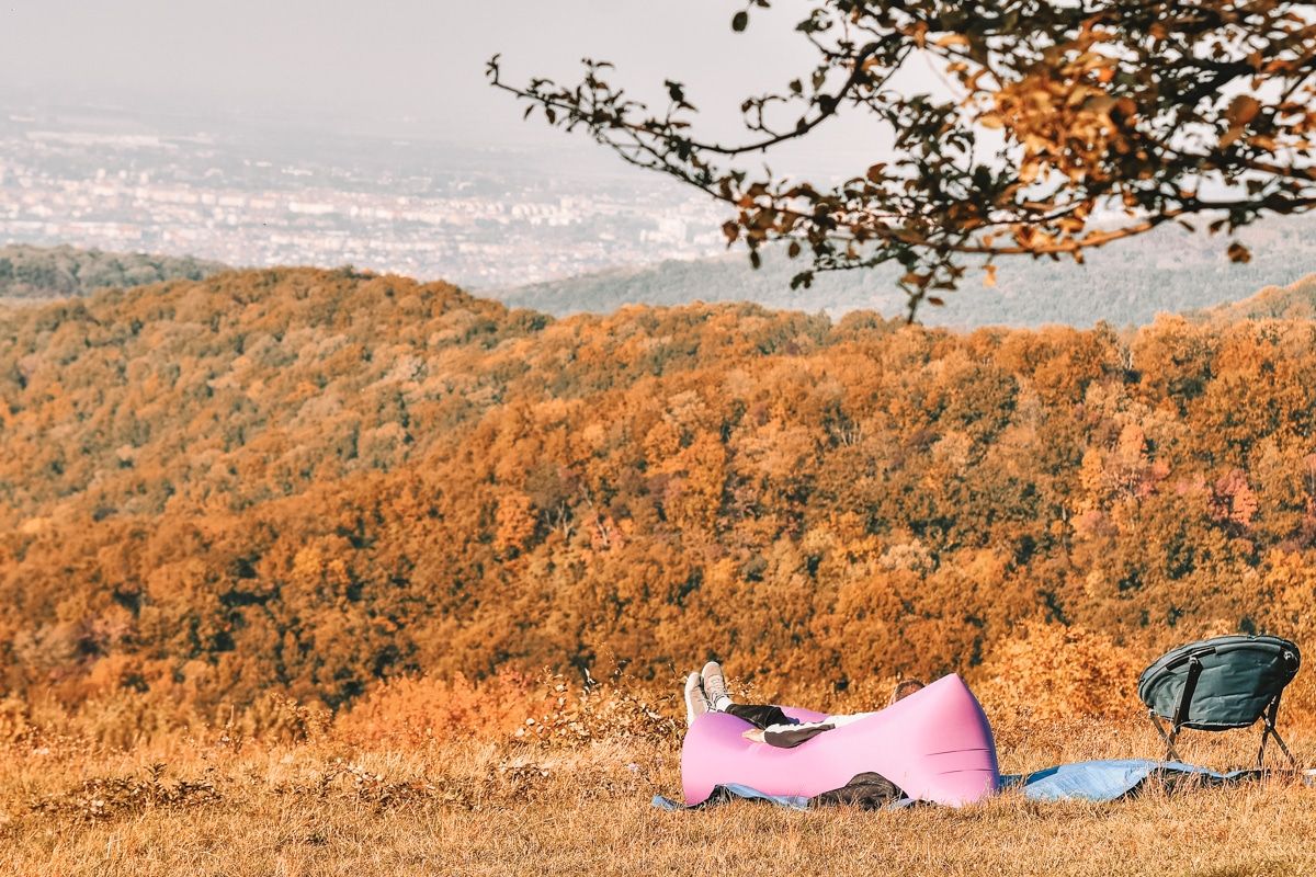 A person's feet visible and they lie on a purple inflatable lounger on a hillside overlooking autumn leaves.