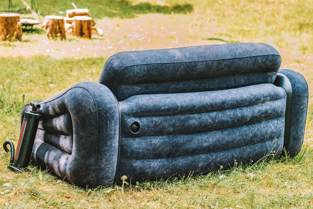 A blue inflatable couch sitting on a grassy field on a sunny day.