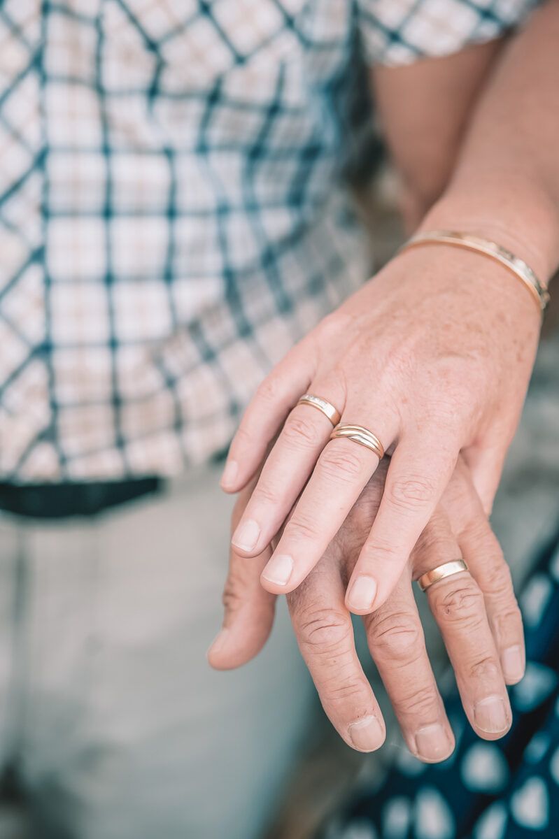 Best 20th Anniversary Gifts: an older woman's hand placed over an older man's hand, both wearing gold wedding rings against a soft focus background.