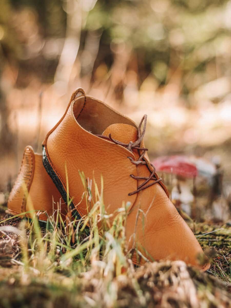 An example of a pair of some of the best barefoot hiking boots in brown leather, posed on a patch of moss and grass.