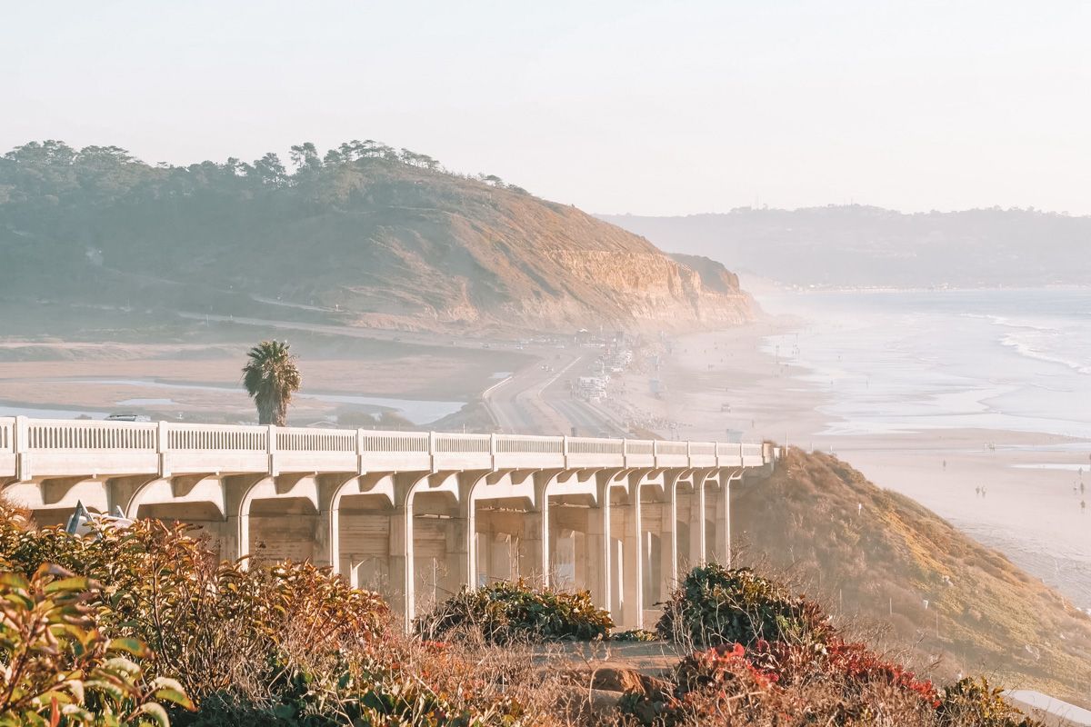 An elevated highway runs alongside a Southern California beach on a hazy, sunny day.