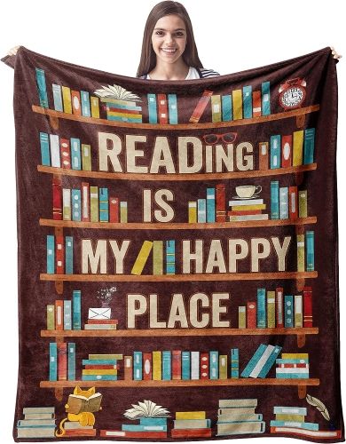 A woman holding up a brown blanket with a drawn image of colorful books on bookshelves and the words "Reading is my Happy Place."