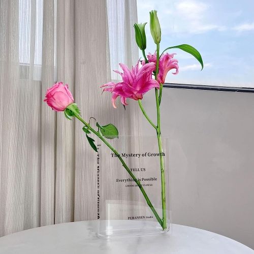 A glass vase shaped like a book holding two pink flowers.