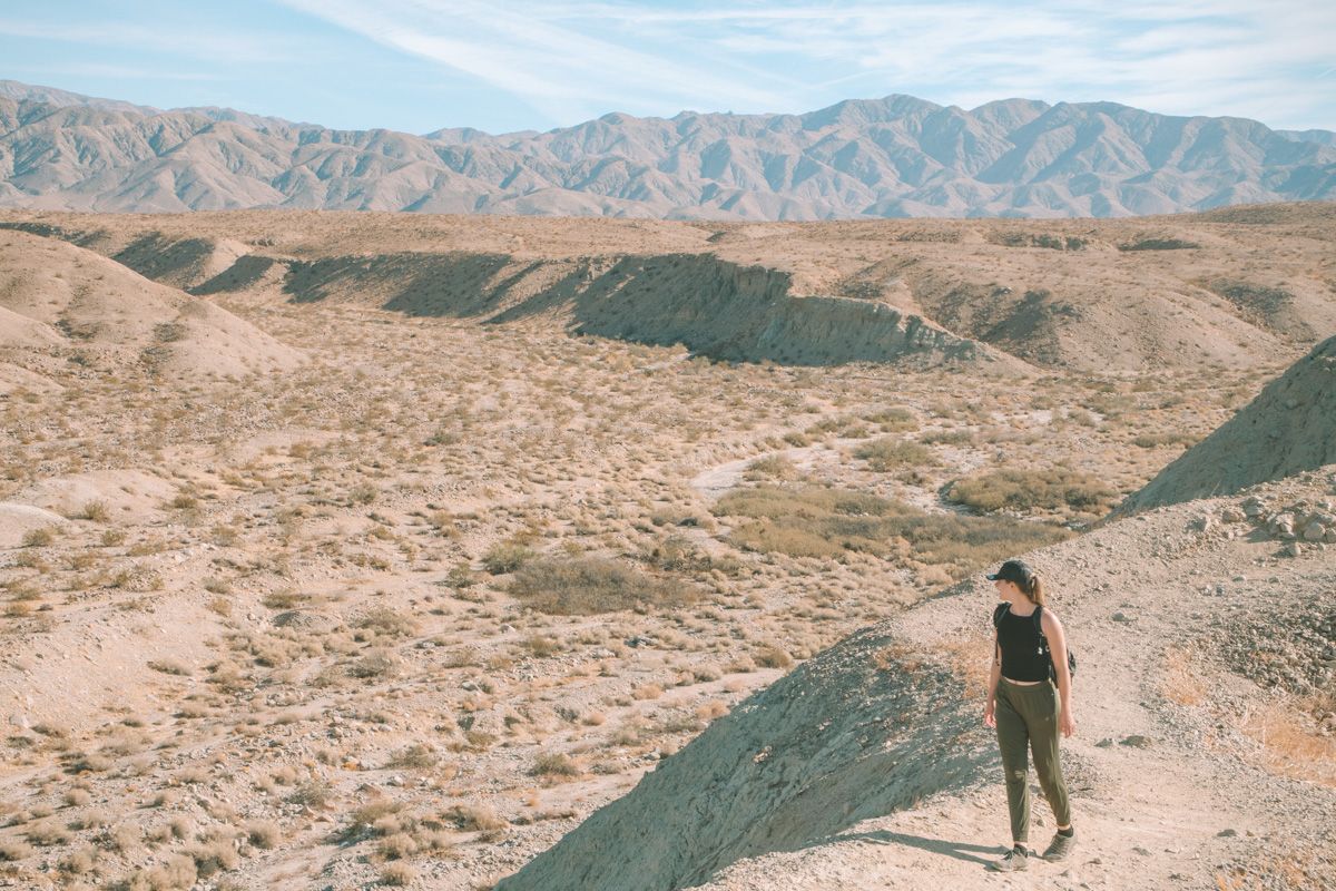 A young woman wearing green pants and a black tank top looking over her shoulder in a desert landscape.