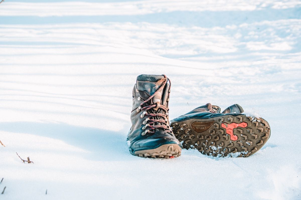 A pair of brown leather barefoot hiking shoes posed in fresh snow.