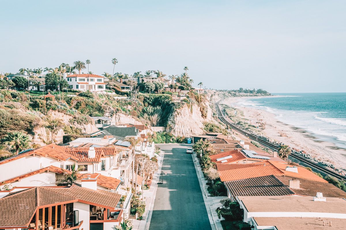 Red-tiled roofs and palm trees interspersed in a San Clemente housing development, with the beach visible beyond them.