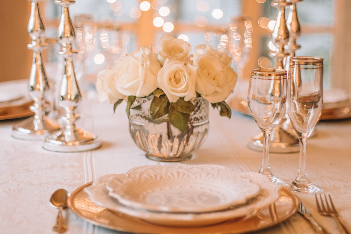 Close-up of a fancy table setting with a white rose bouquet centerpiece and silver candlesticks on the table.