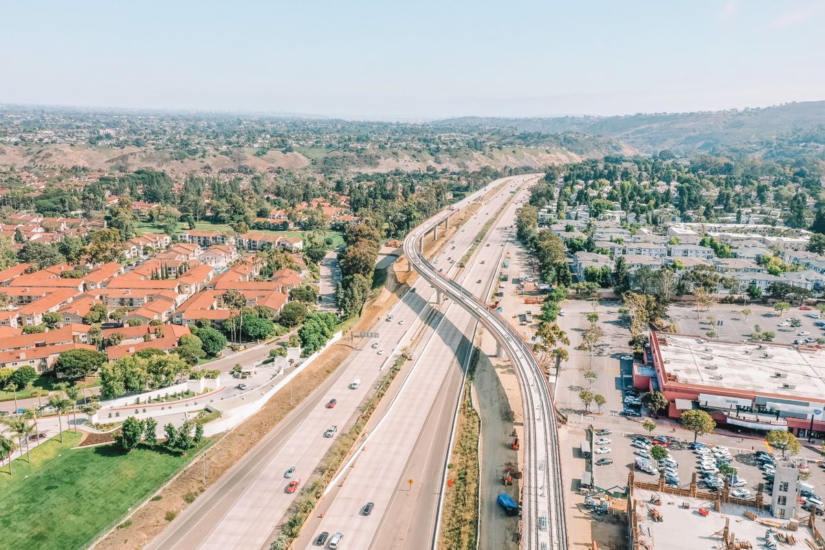 A bird's eye view of a Southern California highway with a shopping center parking lot and a housing development on either side.