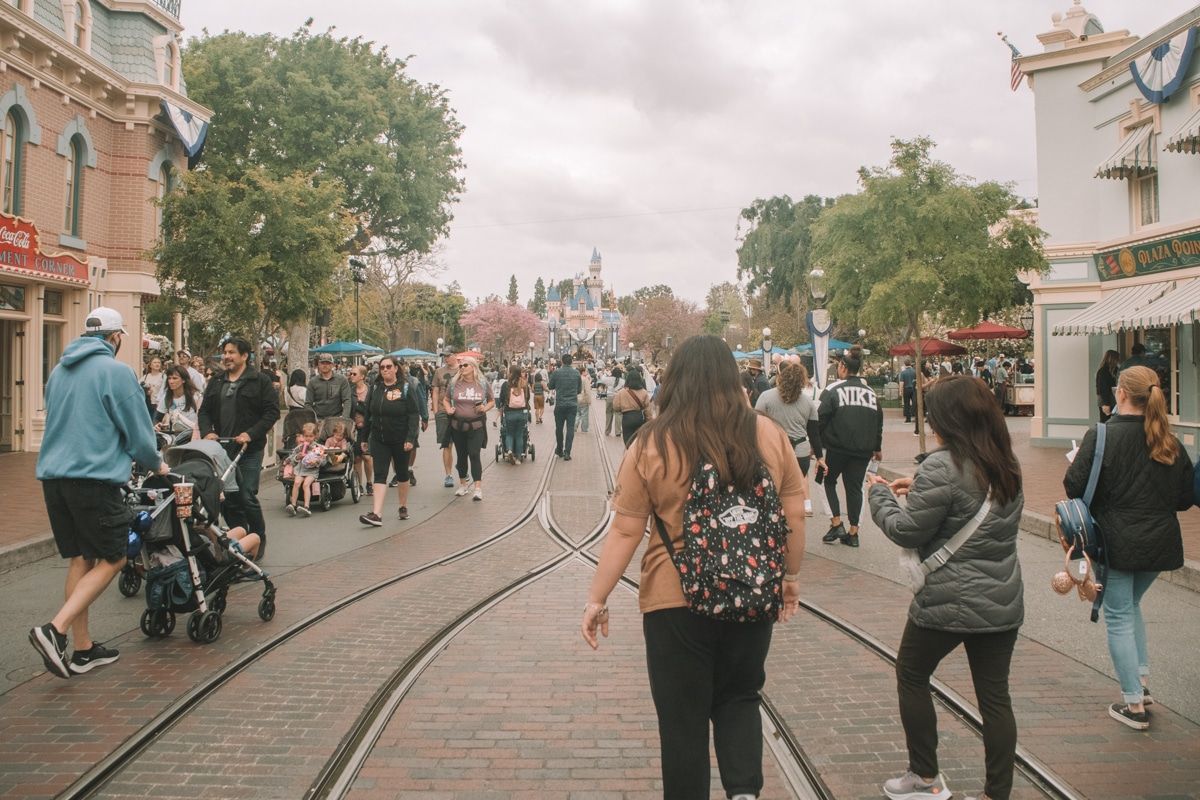Crowds of people walking down the brick-paved road leading into Disneyland on an overcast day.