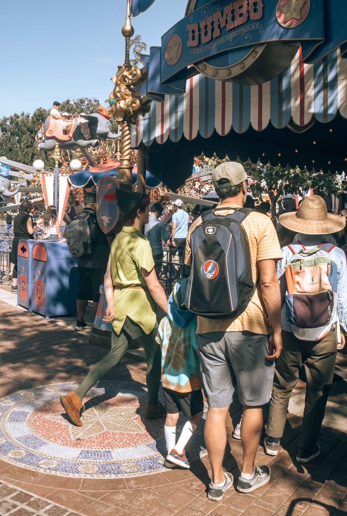 Best Backpacks for Disneyland: two people wearing backpacks, seen from behind, walking with a small boy and a man in a Peter Pan costume at Disneyland.