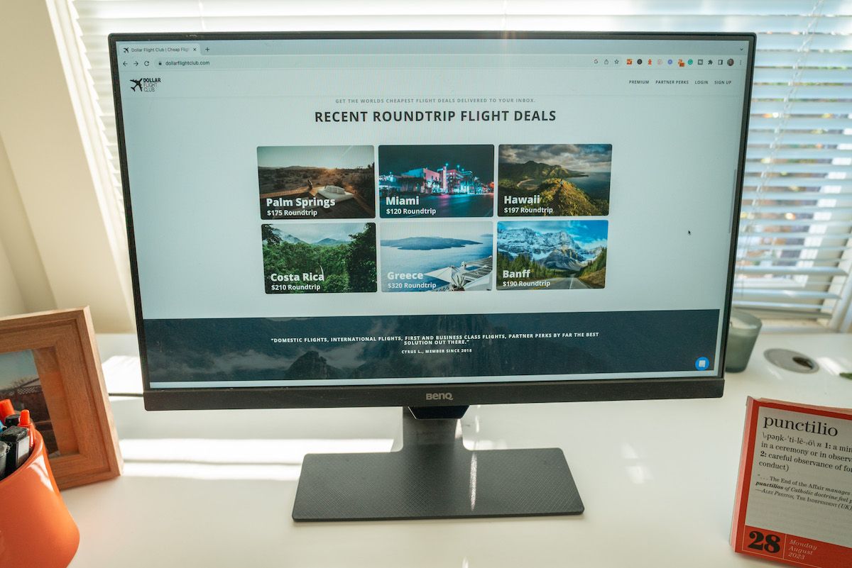 A desktop monitor sitting on a white desk, displaying the Dollar Flight Club website homepage.